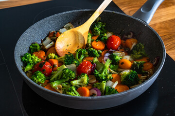Frying mixed vegetables in frying pan on induction cooker	