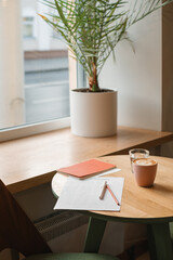 To do list on a table by a window with a notebook, pen, pencil, cappuccino and glass of water.