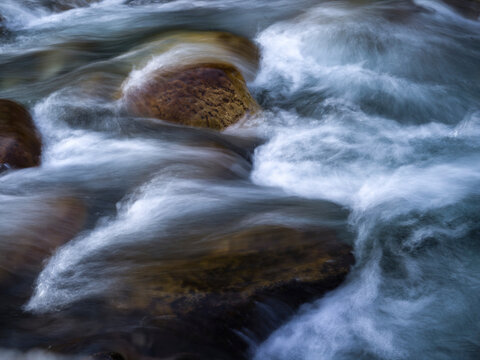 Flowing river over brown rocks with swirling water in a natural setting. Kananaskis, Alberta, Canada