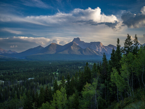 Majestic mountain range under a dramatic sky with lush green forests in the foreground. Kananaskis, Alberta, Canada