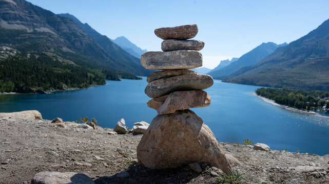 A stack of balanced stones on a hill overlooking a serene lake with mountains in the background. Waterton Park, Alberta, Canada