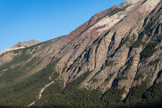 Rugged mountain landscape with steep rocky slopes and sparse greenery under a clear blue sky. Waterton Park, Alberta, Canada