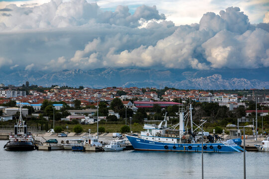 A vibrant commercial harbour with boats docked, Zadar Croatia,, and cloudy mountains in the background.