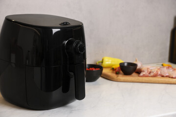 Air fryer, raw chicken thighs, tomatoes and spices on white marble table, closeup