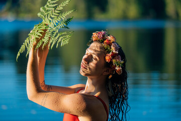 Person in red swimsuit with flower crown holding fern by a serene lakeside. Wildcat Lake Park, WA, USA