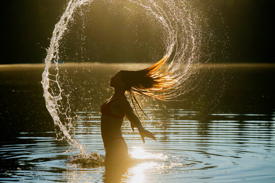 Woman in silhouette flips hair back, creating splash in sunlit water at sunset. Wildcat Lake Park, WA, USA