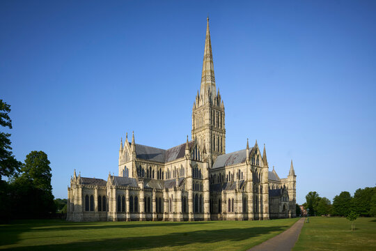 Salisbury Cathedral, majestic cathedral with tall spire under a clear blue sky in lush green surroundings. Salisbury, UK