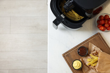 Air fryer, cooked french fries, sauces and tomatoes on white marble countertop, flat lay. Space for text
