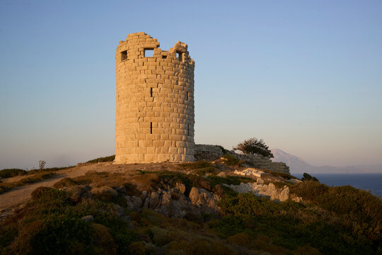 The ancient Greek tower of Drakonon, Ikaria island, Greece. Ancient stone tower on hilltop lit by golden hour sun under a clear sky.