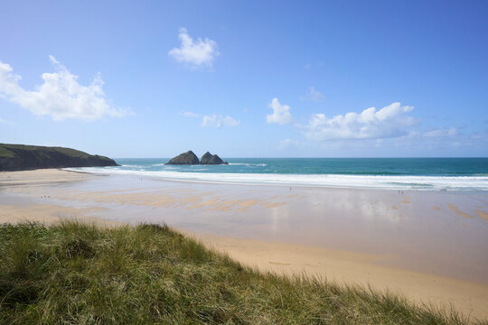 Holywell Bay and beach, Cornwall, UK. Sandy beach with grassy dunes, blue sea, and twin rocks under a clear blue sky.