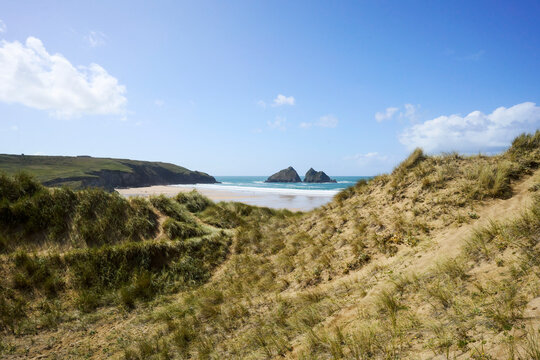 Holywell Bay and beach, Cornwall, UK. Beautiful coastal landscape with sandy dunes and distant rocky islands under a clear blue sky.