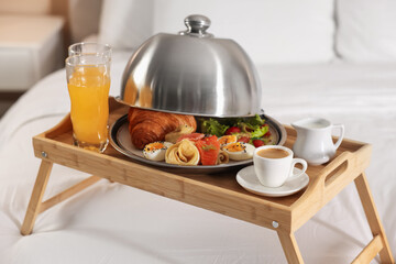 Tray with delicious breakfast on bed in hotel room, closeup