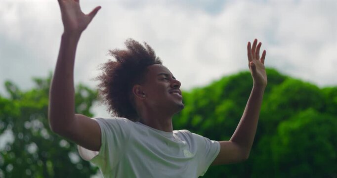 Young African American man smiling and lifting arms in praise, celebrating faith, hope, and emotional release outdoors, symbolizing gratitude and spiritual renewal