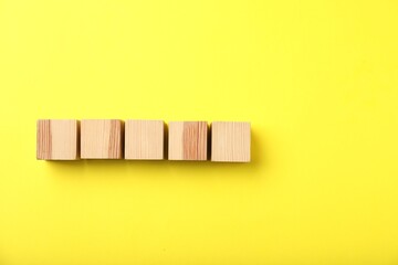 Wooden cubes on yellow background, top view