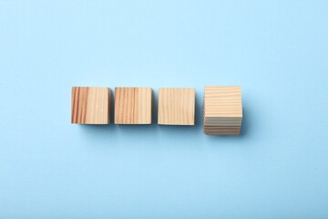 Wooden cubes on light blue background, top view