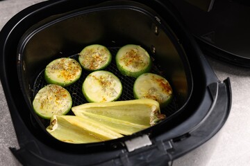 Air fryer basket with grilled vegetables on grey table, closeup