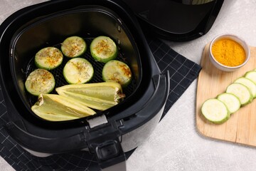 Air fryer basket with vegetables and spices on grey table, above view