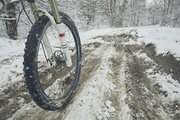 Bicycle wheel rides on a muddy snowy road in the forest in winter
