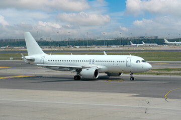 Obraz premium A white commercial airplane is taxiing on the runway at an airport. The scene features a mix of clouds and blue skies, with other planes visible in the background