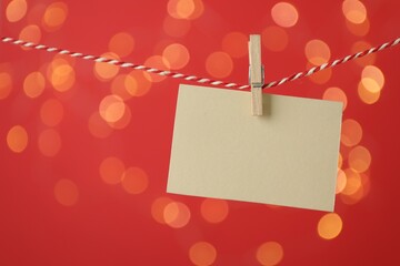 Blank card hanging on string against red background, bokeh effect. Mockup for design