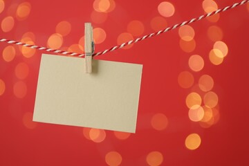 Blank card hanging on string against red background, bokeh effect. Mockup for design