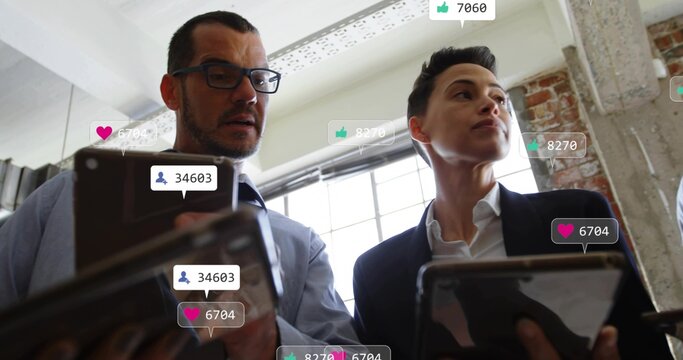 Colleagues in suits holding tablets and viewing social media stats in office with floating icons