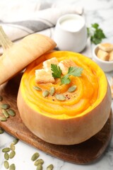 Tasty pumpkin cream soup with seeds, parsley and croutons served in pumpkin on white table, closeup