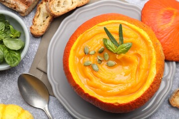 Tasty pumpkin cream soup with seeds and basil served in pumpkin on grey table, flat lay