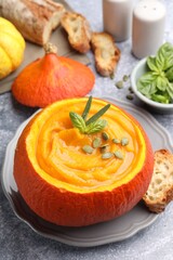 Tasty pumpkin cream soup with seeds and basil served in pumpkin on grey table, closeup