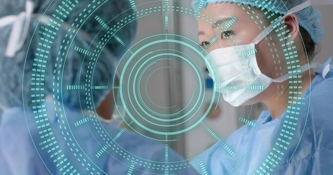 Korean female surgeon scanning AR interface in hospital OR, in blue scrubs, caps and masks