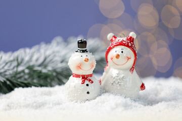 Cute decorative snowman on artificial snow against blue background with blurred lights, closeup