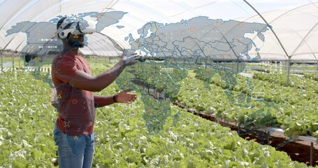 Farmer wearing VR headset holding controllers navigating map in greenhouse, with lettuce trays