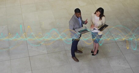 Obraz premium Reviewing colleagues in suits analyzing laptop and folder in lobby, with waveform graph overlay