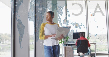 Standing office woman holding laptop, glancing right in office with park view, world map overlay