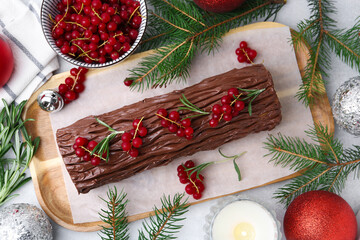 Delicious Yule log (traditional Christmas cake) with redcurrant, decor and fir tree branches on light table, flat lay