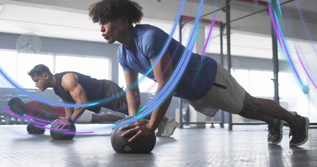 Doing push-ups man in athletic clothes balancing on medicine ball in gym room with pull-up rig