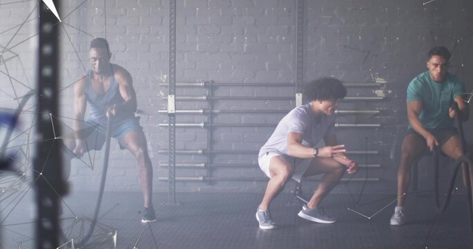 Instructor guiding clients wearing workout clothes waving battle ropes in gym, with barbell racks