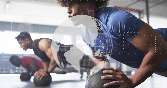 Performing push-up man wearing blue shirt on black medicine ball on rubber gym floor, copy space