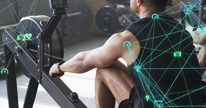 Pulling man wearing black sleeveless top rowing ergometer near weight plates in modern gym