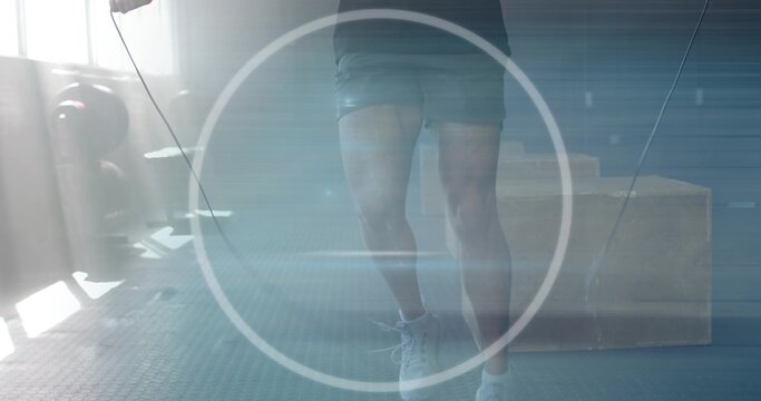 Lower body of man in athletic shorts, sneakers skipping rope in fitness studio, with plyometric box