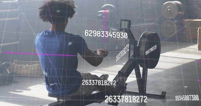 Rowing man in blue sportswear pushing handle at gym, with digital display and towel basket