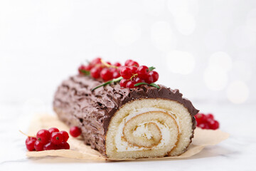 Delicious Yule log (traditional Christmas cake) with redcurrant on white table, closeup