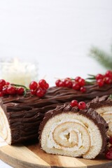 Delicious Yule log (traditional Christmas cake) with redcurrant on white table, closeup. Space for text