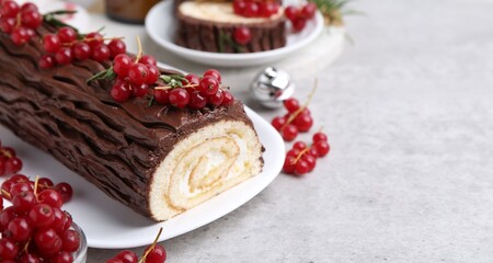 Delicious Yule log (traditional Christmas cake) with redcurrant on gray textured table, closeup. Space for text