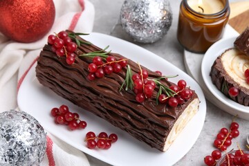 Delicious Yule log (traditional Christmas cake) with redcurrant and decor on gray table, closeup