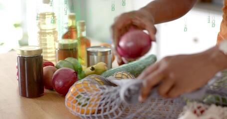 Hands placing red onion into reusable mesh bag on home kitchen countertop, with glass oil jars © vectorfusionart