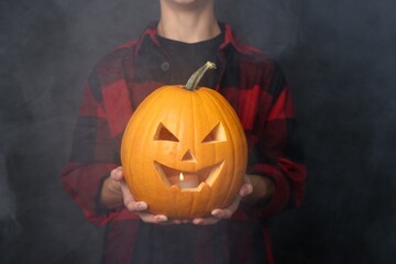 Halloween celebration. Boy with jack o'lantern pumpkin on black background with smoke, closeup