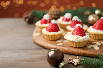 Christmas food. Tasty tartlets with strawberries, whipped cream, coconut flakes and decor on wooden table against background with blurred lights, space for text. Bokeh effect