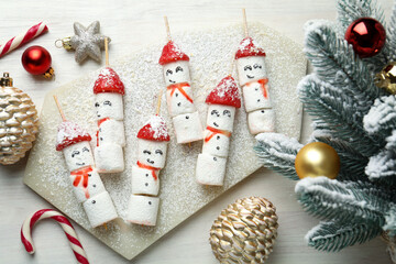 Christmas food. Funny snowmen made of marshmallows, strawberries and decor on wooden table, flat lay