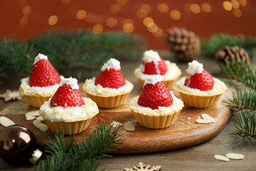 Christmas food. Tasty tartlets with strawberries, whipped cream, coconut flakes and decor on wooden table against background with blurred lights, closeup. Bokeh effect